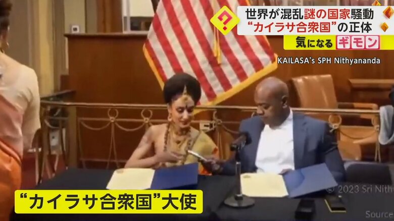 姉妹都市提携の書類にサインをしている“カイラサ合衆国”大使とスーツ姿の男性