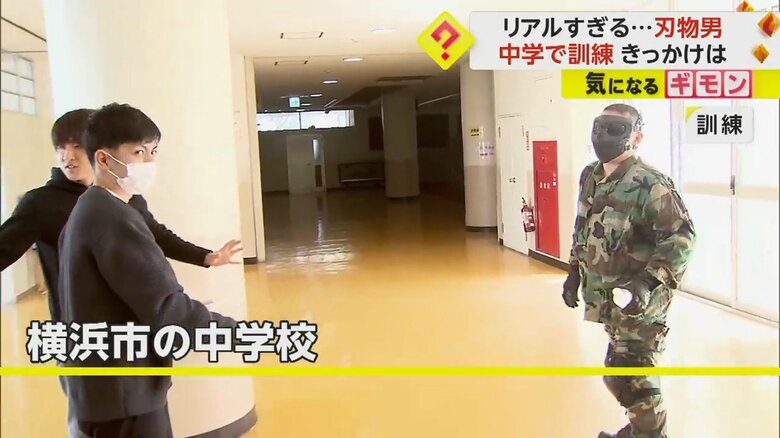 覆面姿の男と教職員が向かい合っている