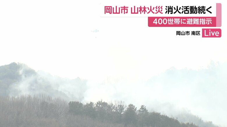 24日午前11時半すぎの様子。画面中央上部に、煙の中で消火活動を行うヘリコプターが見える（岡山市）