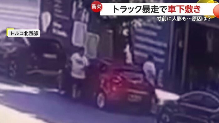 赤い車を挟んで立つ2人の人物(IHA)