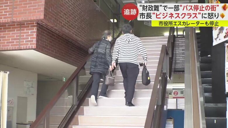 エスカレーターが停止中のため手すりをつかみながら階段を登る高齢者