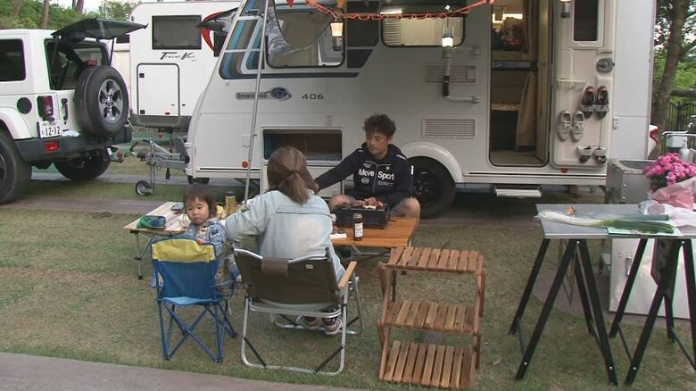 キャンピングカーの隣でバーベキューを楽しむ家族