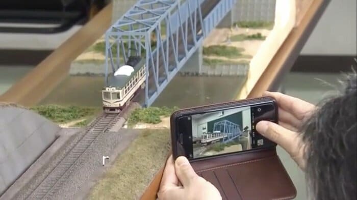 ジオラマの鉄橋を渡る模型を撮影するメンバー