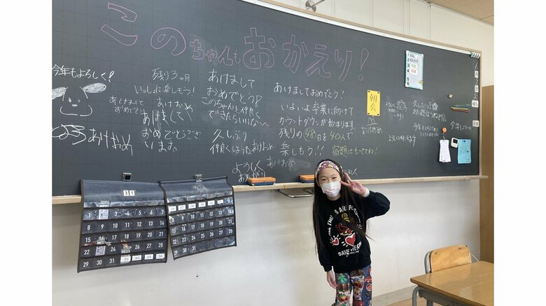 黒板に書かれた「おかえり」メッセージの前でピース