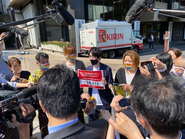 自民党本部前で会見する松岡宗嗣さん（署名数のプラカードを持つ）