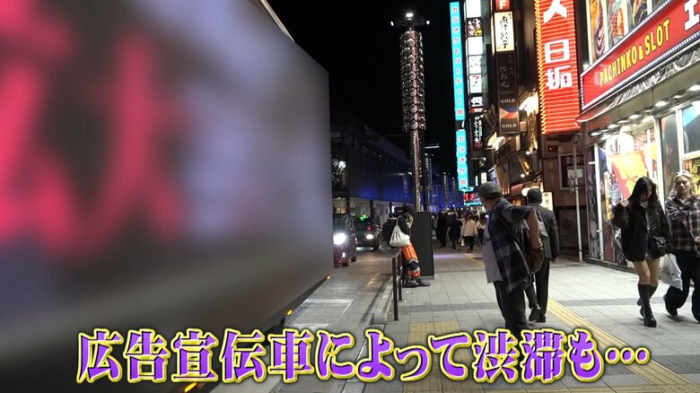 ゆっくりと走る広告宣伝車　後ろには車の列が