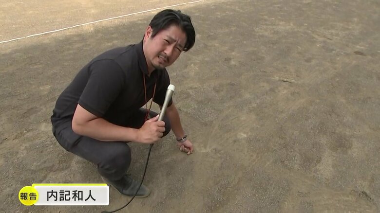 内記和人記者が事故のあったグラウンドの地面の砂を触って確認している