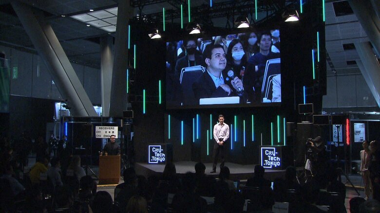 中央に立つプレゼンターに審査員（大画面）が質問