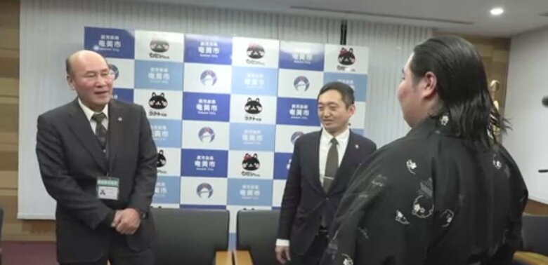 相撲甚句で祝福する奄美市・向美芳教育長（左）。中央は安田壮平市長