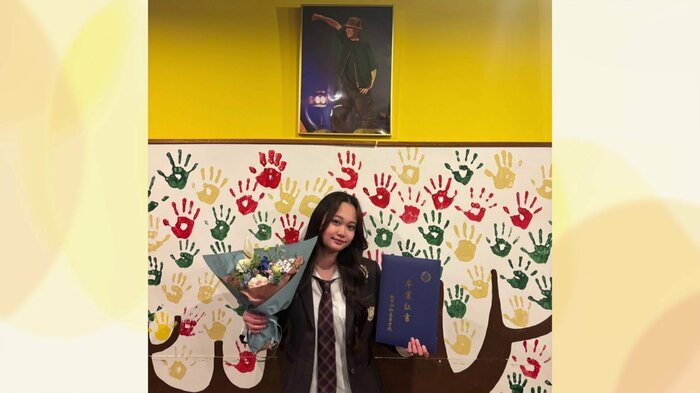 卒業証書を手にスタジオに飾る阿部さんの写真の下で記念撮影する保坂さん