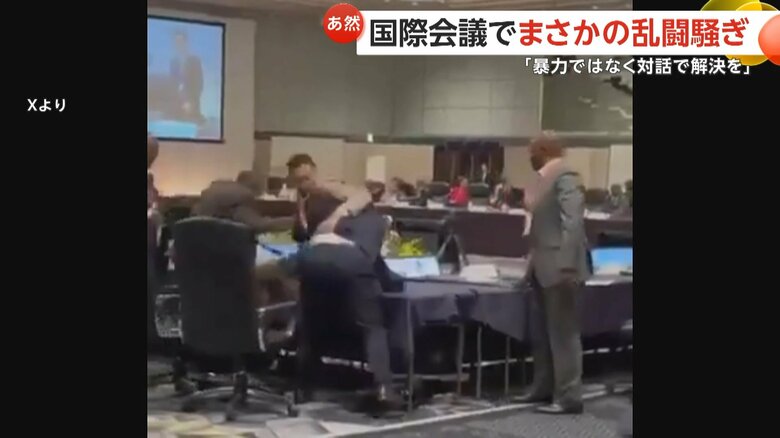 ベージュのスーツの男性に背中から飛び掛かる紺色のスーツの男性