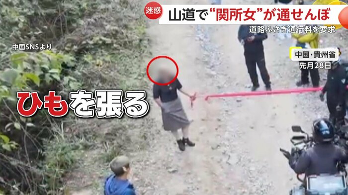 道路に赤い紐を張る女