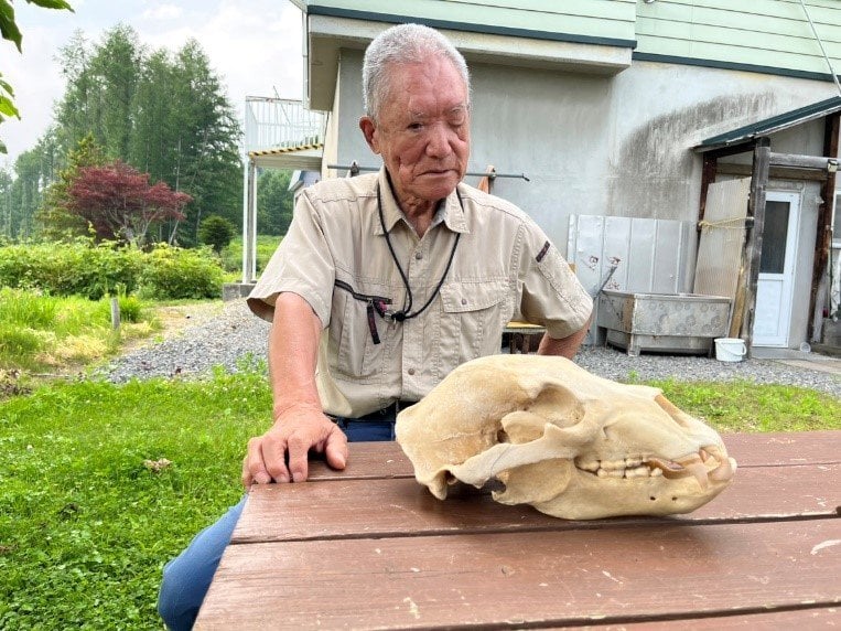 襲われた当時の様子を話す原田さん（手元にあるのは実際に襲ってきたクマの頭蓋骨）