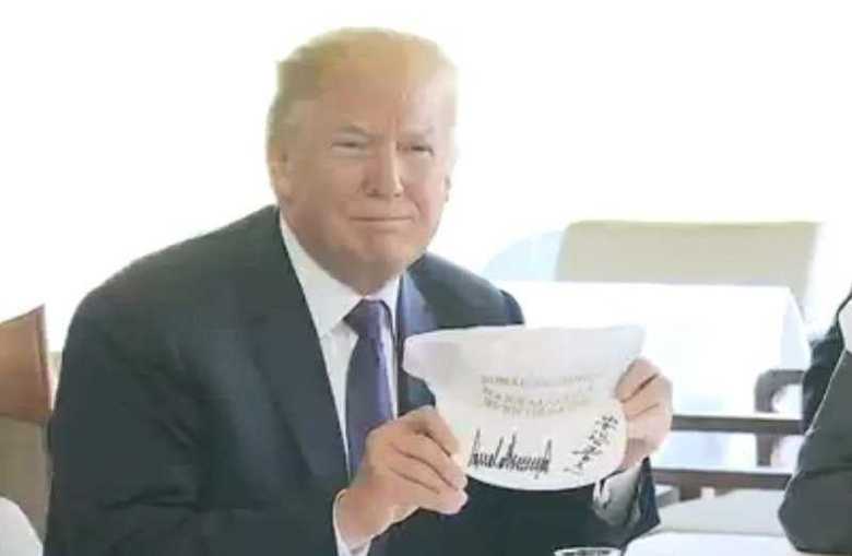 記念品の白いゴルフキャップにサインをしたトランプ大統領