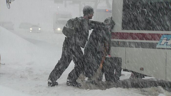 雪にハマったバスを押す観光客たち