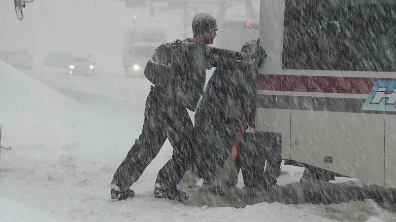 雪にハマったバスを押す観光客たち
