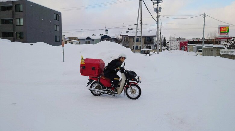 雪山のある交差点で注意深く安全確認する郵便局員
