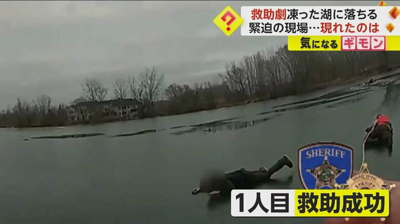 岸からロープでたぐり寄せられた男性と警察官