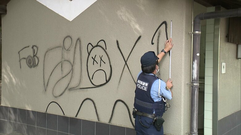 トイレ壁面の落書きの状況を調べる警察官
