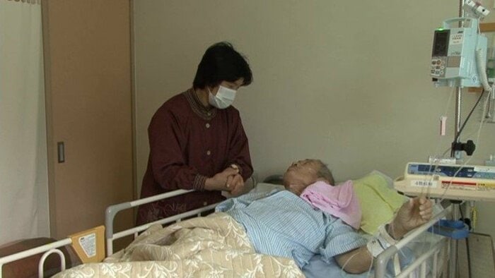 病床で益代さんの手を握るトラさん