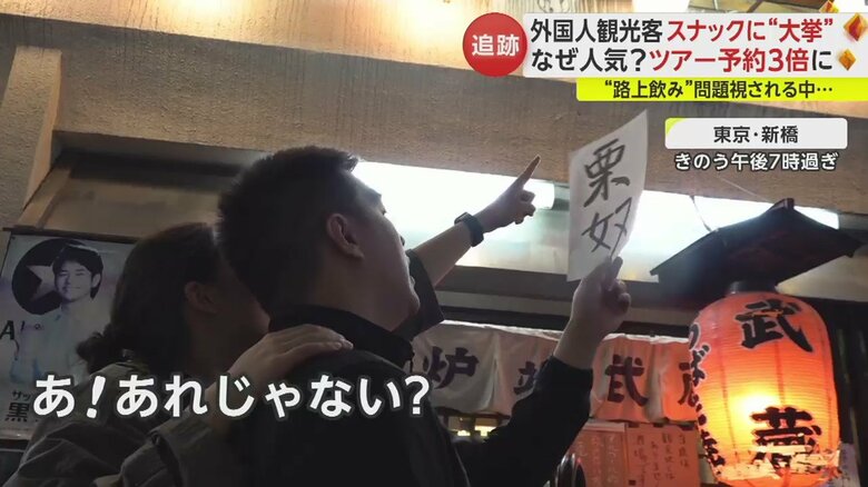 スナックに入る前、漢字の店名が書かれた紙を手に店を探す2人