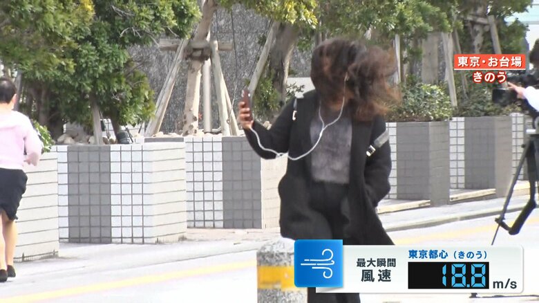 強風で髪の毛が顔を覆いよろめく女性