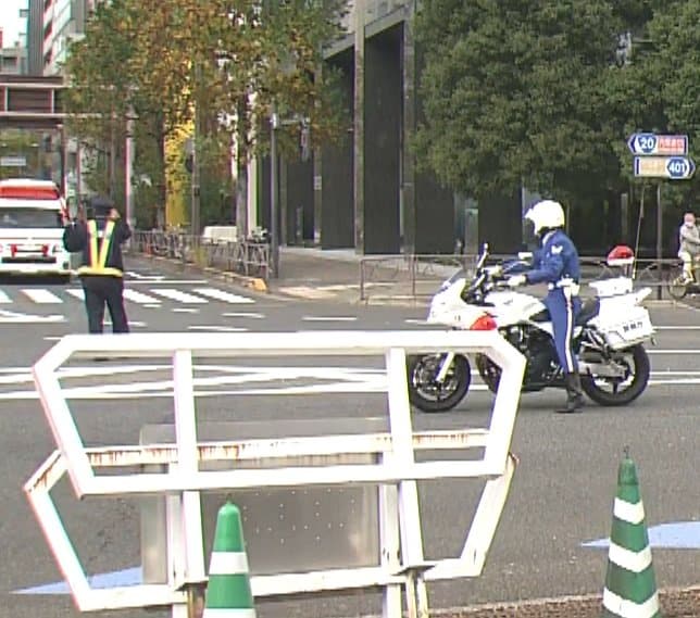 陛下の車列を先導する白バイは一時停止、奥から来る救急車を先に誘導する警察官（28日）