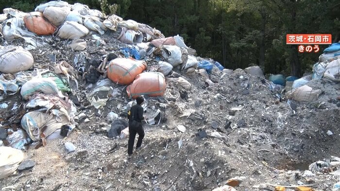 山のようにつまれた産廃物の山を登る取材スタッフ