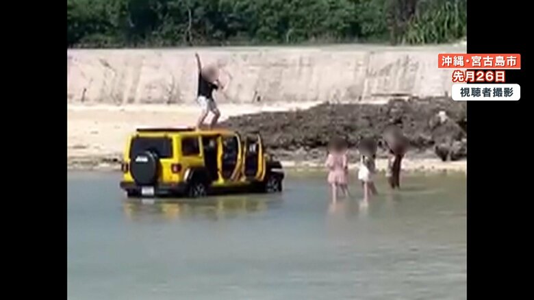 男性がポーズを取っている車が止められているのは、海の中