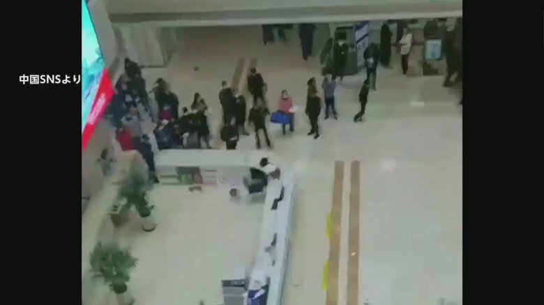 病院のロビーで人々が棒を持った女性を見つめている