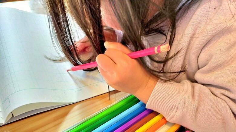 お地蔵様が彫られた鉛筆を使う娘さん