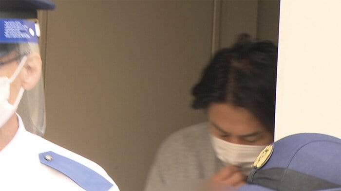 河合容疑者は、報道カメラを目にすると、サッとマスクを広げて、顔を隠した(7日 築地署)