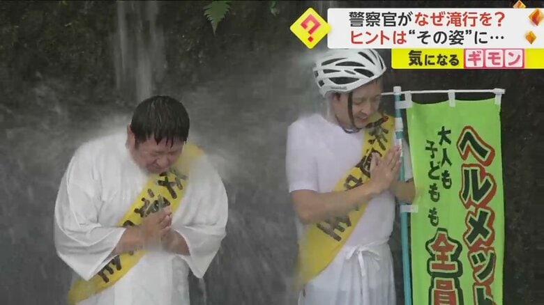 白装束を着て、交通安全のたすきをかけながら滝に打たれる警察官