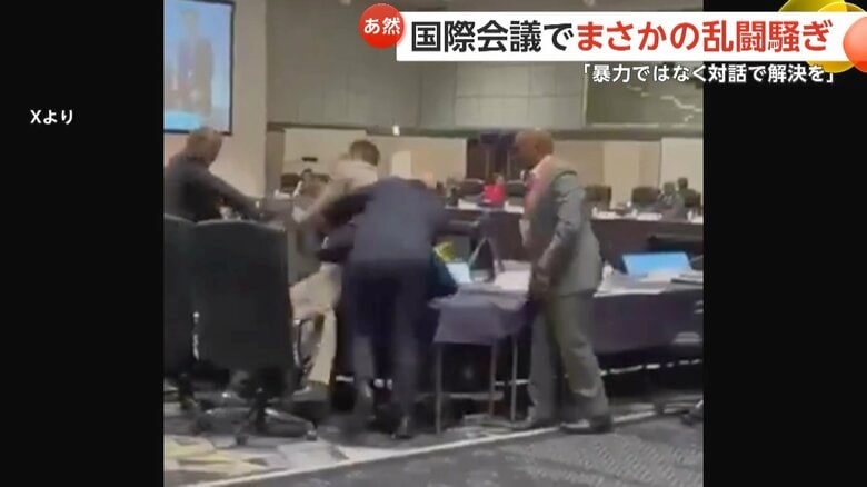 ベージュのスーツの男性に背中から飛び掛かる紺色のスーツの男性