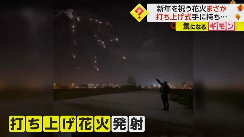 打ち上げ花火を手に持つ男性が、夜空に向けて花火を発射している