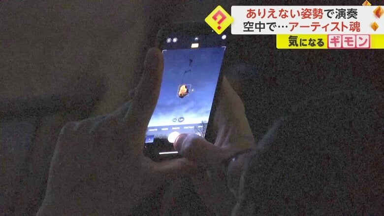 宙に浮いたピアノを携帯で撮影する人