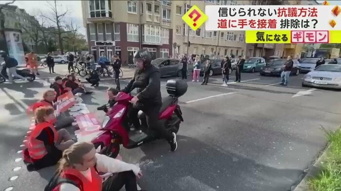 座り込む環境活動家たちの間をすり抜けていくバイク