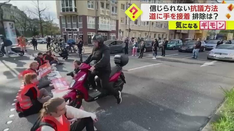 座り込む環境活動家たちの間をすり抜けていくバイク
