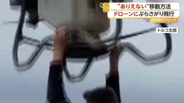 ドローンの下部にあるバーにつかまる男性（IHA）