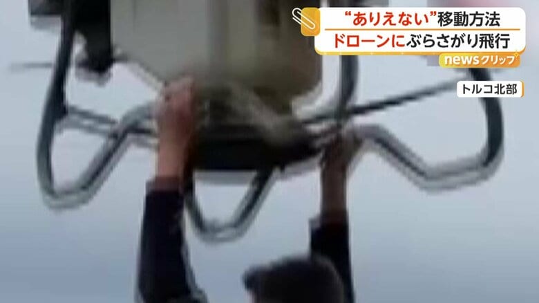 ドローンの下部にあるバーにつかまる男性（IHA）