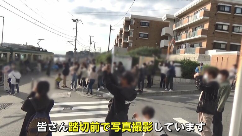 海の見える踏切前でカメラを構える人々