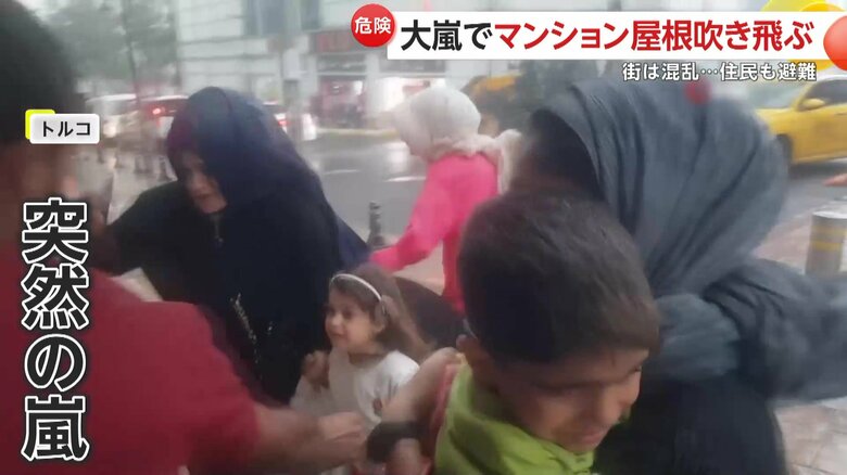 突然の嵐に体を屈めながら、建物の中へと避難する人たち