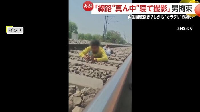線路上の真ん中でうつ伏せになる男