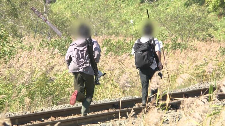 三脚やカメラのようなものを抱え、線路を走る2人組
