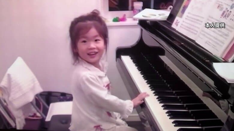 ピアノの前で笑顔を見せる幼少期の伊藤さん