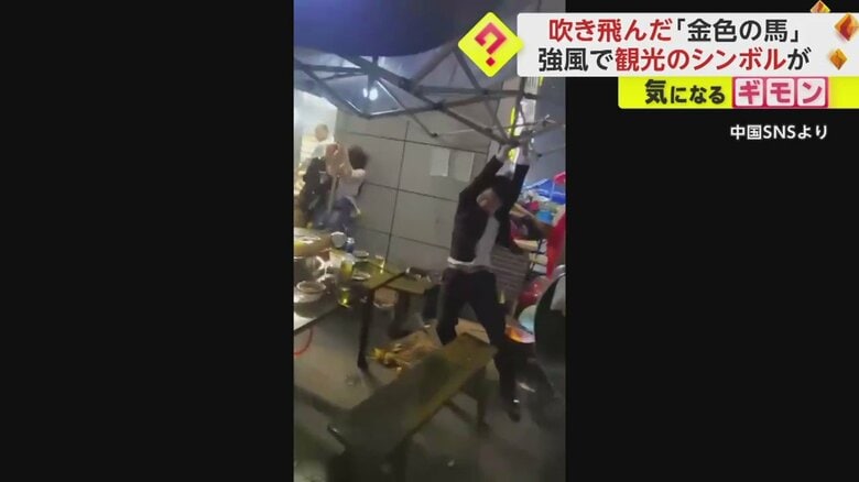 吹き飛ばされそうになるテントを必死に押さえる人