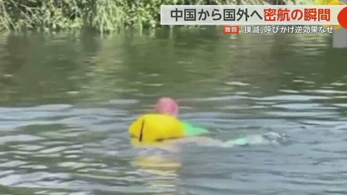 袋を浮輪代わりに向こう岸まで懸命に泳いでいく女性