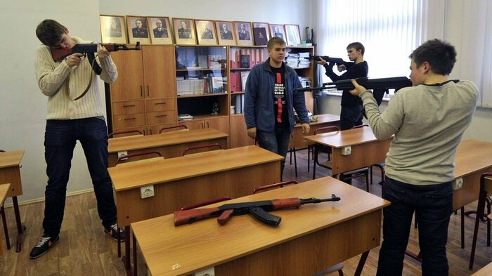 写真説明=教室で小銃を構えるロシアの高校生。小銃の分解・組み立てを学び、友だちを敵に見立て、銃口を向ける(2023年、ロシア反体制メディアより)