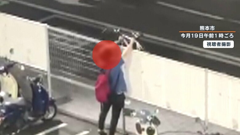駐輪場のフェンス際で自転車を持ち上げる男性