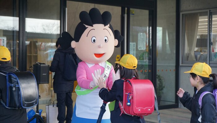 登校時、玄関先で出迎えるサザエさんとハイタッチする小学生(志賀小学校)